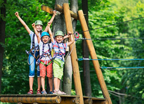 three kids smiling with their arms up proud to be completing an adventure course